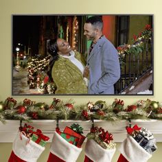 a couple standing next to each other in front of christmas stockings with presents hanging from them