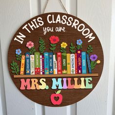 a wooden sign that says in this classroom you are mrs millie with books and flowers