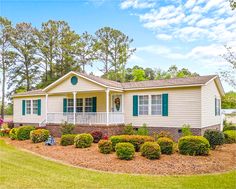 a white house with green shutters on the front porch and landscaping around it, surrounded by trees