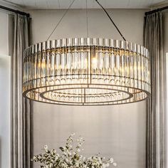 a chandelier hanging over a dining room table with flowers in the vase on it