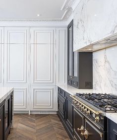 an elegant kitchen with marble counter tops and black ovens, along with herringbone wood flooring