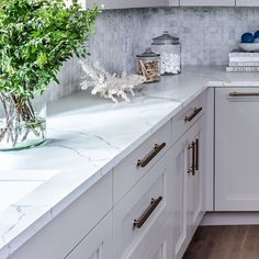 a kitchen with white cabinets and marble counter tops, along with a vase filled with flowers