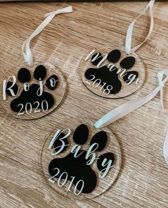 three ornament shaped like dogs with their names on them, hanging from a wooden table