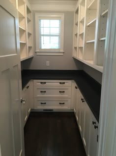 an empty kitchen with white cabinets and black counter tops, along with dark wood flooring