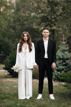 a man and woman in formal wear standing next to each other on grass with trees in the background