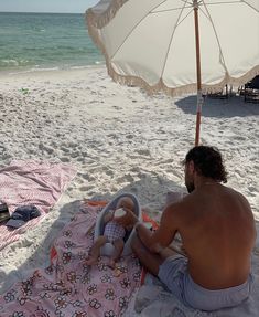 a man sitting on top of a beach next to an umbrella