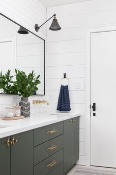 a white bathroom with green cabinets and gold handles on the vanity, along with a large mirror