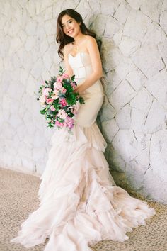 a woman in a wedding dress leaning against a wall holding a bouquet of pink flowers