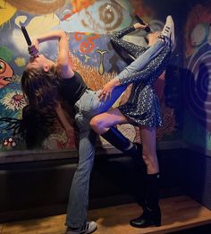 two young women are dancing in front of a wall with graffiti on it and one is holding an umbrella