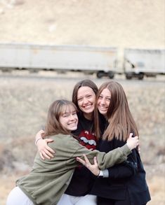 three girls hugging each other in front of a train