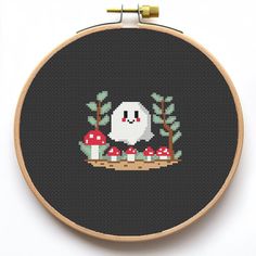 a cross stitch pattern with a white ghost and mushrooms on black background, in a round wooden frame