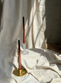 two candles sitting on top of a white cloth covered floor next to a glass candle holder