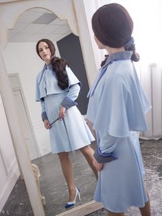 a woman standing in front of a mirror wearing a blue dress and high heeled shoes