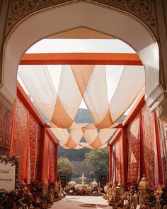 an outdoor ceremony with orange drapes and flowers on the aisle, surrounded by white pillars