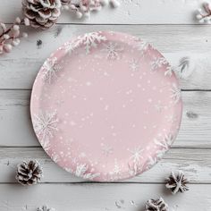 a pink plate with white snowflakes and pine cones around it on a wooden table