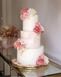 a three tiered cake with pink and white flowers on the top, sitting on a table