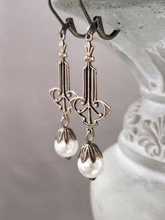 These 1920s inspired pearl dangles feature Deco style dark bronze brass connectors and luminous white glass pearl beads. The lightweight yet sturdy brass connectors are textured on the front and slightly hollow on the back. (SEE 2nd Photo)  These earrings measure 2 1/4 inches long and hang from antique brass lever back ear wires. ABOUT THIS COLLECTION The sophisticated style of the Roaring Twenties is timeless. The sparkling crystal and luminous pearl jewels in this collection are perfect for your 1920s inspired wedding or just your everyday wardrobe. I invite you to browse my complete 1920s Bride Collection here: https://www.etsy.com/shop/BohemeBijou?ref=l2-shopheader-name&section_id=18080838 Elegant Brass Earrings With Antique Finish, Antique Finish Bronze Wedding Earrings, Antique Bronze Earrings For Wedding, Victorian Wedding Earrings With Antique Finish, Elegant Antique Finish Bronze Jewelry, Elegant Nickel-free Brass Pearl Earrings, Vintage Metal Pearl Earrings For Wedding, Vintage Nickel-free Pearl Earrings For Wedding, Vintage White Pearl Pierced Earrings