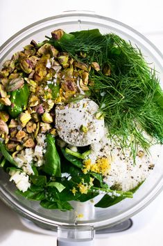 a glass bowl filled with green vegetables and other food items on top of a white table