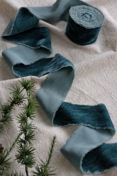 two rolls of blue fabric sitting on top of a white cloth covered in pine needles