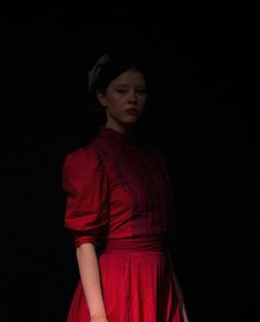 a woman in a red dress is holding a white purse and standing against a black background