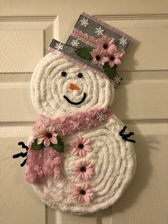 a snowman door hanger with pink flowers and a hat on it's head