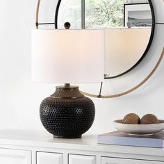 a table lamp sitting on top of a white dresser next to a mirror and bowl