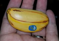 a hand holding a small yellow banana with blue stickers on it's side