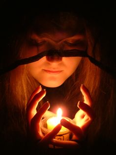 a woman holding a candle in her hands with the light shining on her face behind her