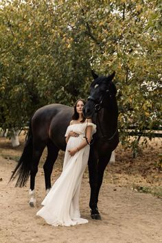 a pregnant woman standing next to a black horse