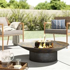 a fire pit sitting on top of a patio next to two chairs and a table