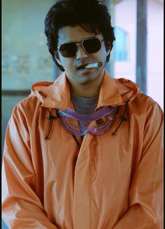 a man in an orange jacket with sunglasses on his face and a toothbrush in his mouth