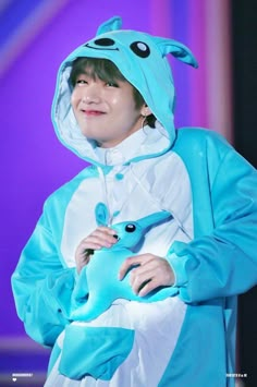 a boy in a blue costume holding a stuffed animal and smiling at the camera while standing on stage