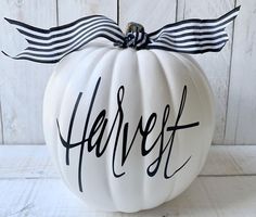 a white pumpkin with black lettering on it and a bow tied around the top that says harvest