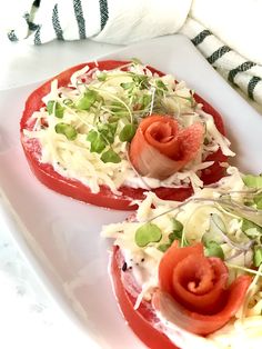 two slices of tomato topped with cheese and veggies on a white platter