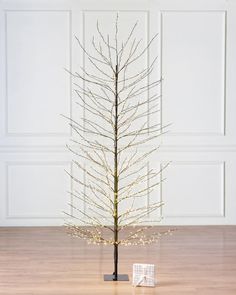 a small christmas tree with white lights on it in front of a wall and wooden floor