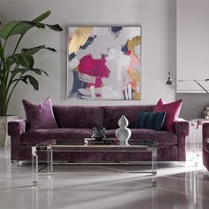 a living room filled with purple furniture next to a large painting on the wall above a glass coffee table