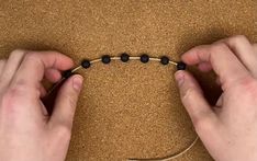 two hands stringing a beaded bracelet with black beads on a brown surface,