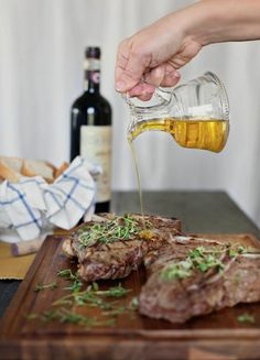 a person pouring olive oil over steak on a cutting board