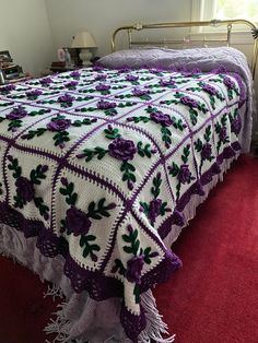 a crocheted bedspread with purple and green flowers on it in a bedroom