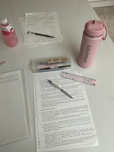 a table topped with papers and pens next to a pink cup on top of it