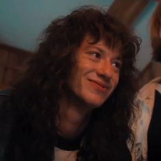 a man with long curly hair is smiling at the camera while another person looks on