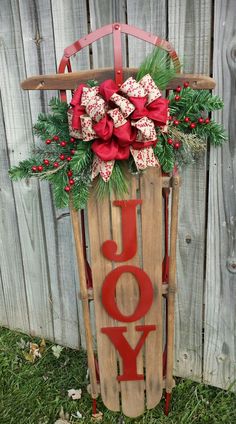 a wooden sled with the word joy in red and green decorations on it sitting next to a fence