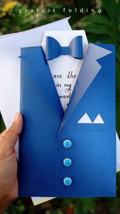 a hand holding an origami card with a blue suit and bow tie