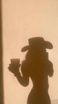 the shadow of a person wearing a hat and holding a cup