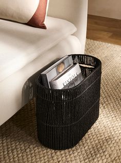 a black basket sitting on top of a rug next to a white couch and pillows