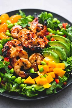 a black plate topped with shrimp and veggies next to avocado wedges