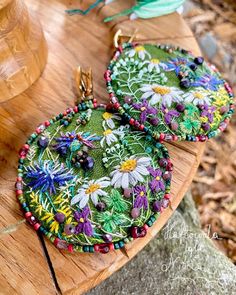 two circular earrings with flowers on them sitting on top of a wooden table next to a vase