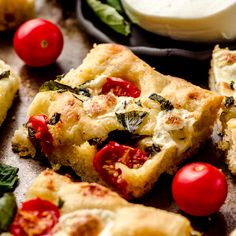 several pieces of pizza with tomatoes and spinach on the table next to some dip