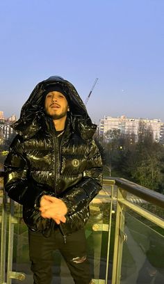 a man standing on top of a balcony next to a glass railing with his hands in his pockets