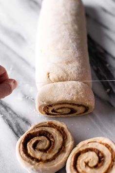 a person holding a piece of bread with cinnamon swirls on it and another roll in the background